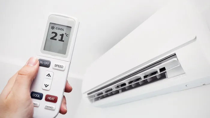 Hand hält Klimaanlagenfernbedienung auf 21 °C neben Wandgerät