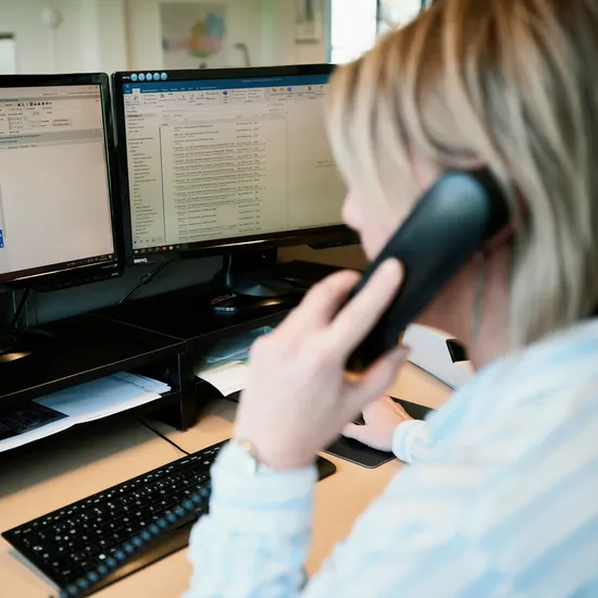 Frau am Schreibtisch nutzt Computerkalender und Telefon im Büro