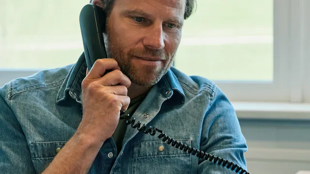 Mann im Jeanshemd telefoniert und hält Papiere im Büro
