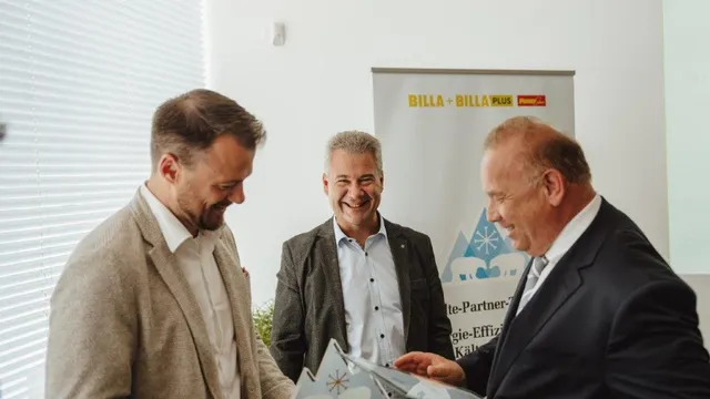 Drei Geschäftsleute teilen Dokumente vor einem Billa Plus Banner