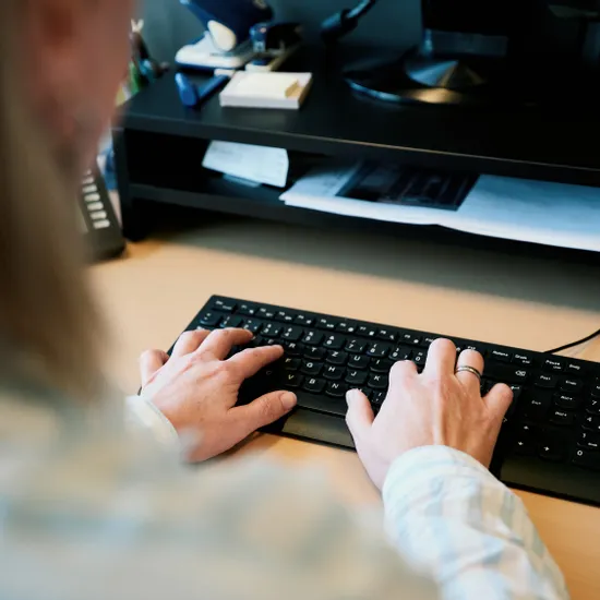 Person tippt auf einer Computertastatur an einem Holztisch