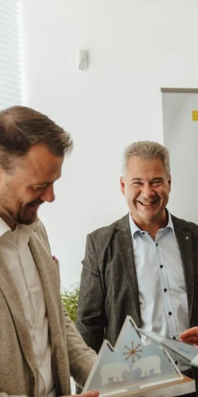 Drei Geschäftsleute teilen Dokumente vor einem Billa Plus Banner