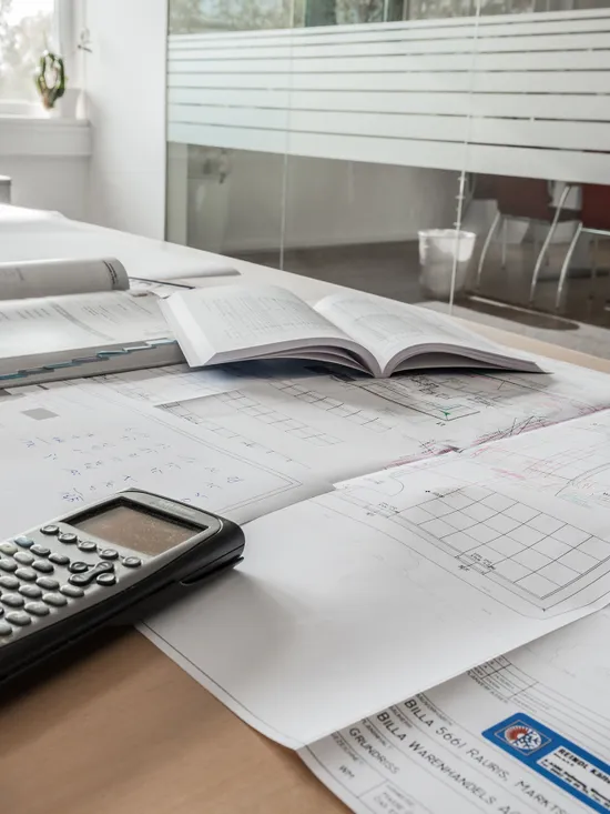 Architektenpläne mit Taschenrechner und offenen Büchern auf Schreibtisch