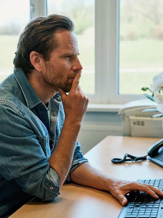 Mann im Jeanshemd arbeitet am Computer in einem hellen Büro