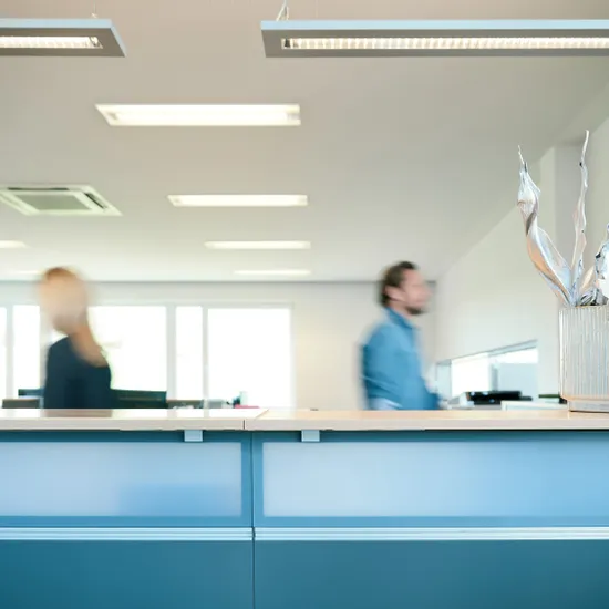 Empfangstresen in modernem Büro mit unscharfen Personen und Dekopflanze