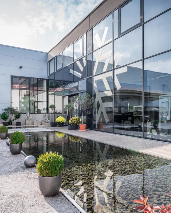 Moderne Gebäudefassade mit großen Glasfenstern, die einen Hof mit Pflanzen und Teich spiegeln
