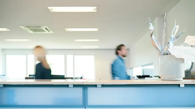 Empfangstresen in modernem Büro mit unscharfen Personen und Dekopflanze