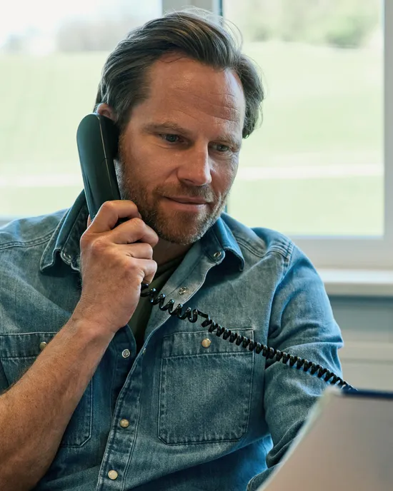 Mann im Jeanshemd telefoniert und hält Papiere im Büro