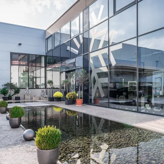 Moderne Gebäudefassade mit großen Glasfenstern, die einen Hof mit Pflanzen und Teich spiegeln