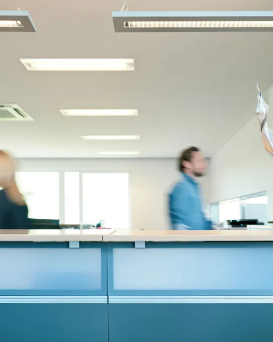 Empfangstresen in modernem Büro mit unscharfen Personen und Dekopflanze