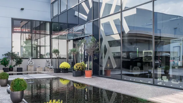 Moderne Gebäudefassade mit großen Glasfenstern, die einen Hof mit Pflanzen und Teich spiegeln