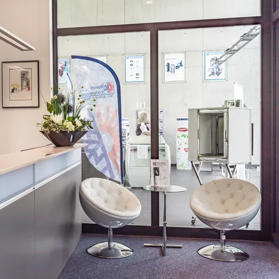 Moderne Bürorezeption mit Blumenarrangements, Stühlen und Werbebanner